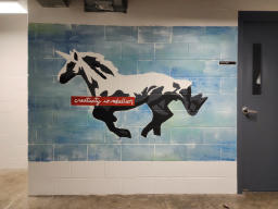 A white, grey, and black posterized depiction of a unicorn on a light blue and
green background. In front of the unicorn's chest there is a red box with white
cursive writing over it that says 