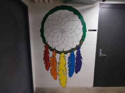 A mural of a dream catcher with a woven string web in the center and five
different colored feathers hanging from the bottom. The dream catcher itself is
brown with a green string wrapping around the top section. The feathers, from
left to right, are red, orange, yellow, blue, and purple.