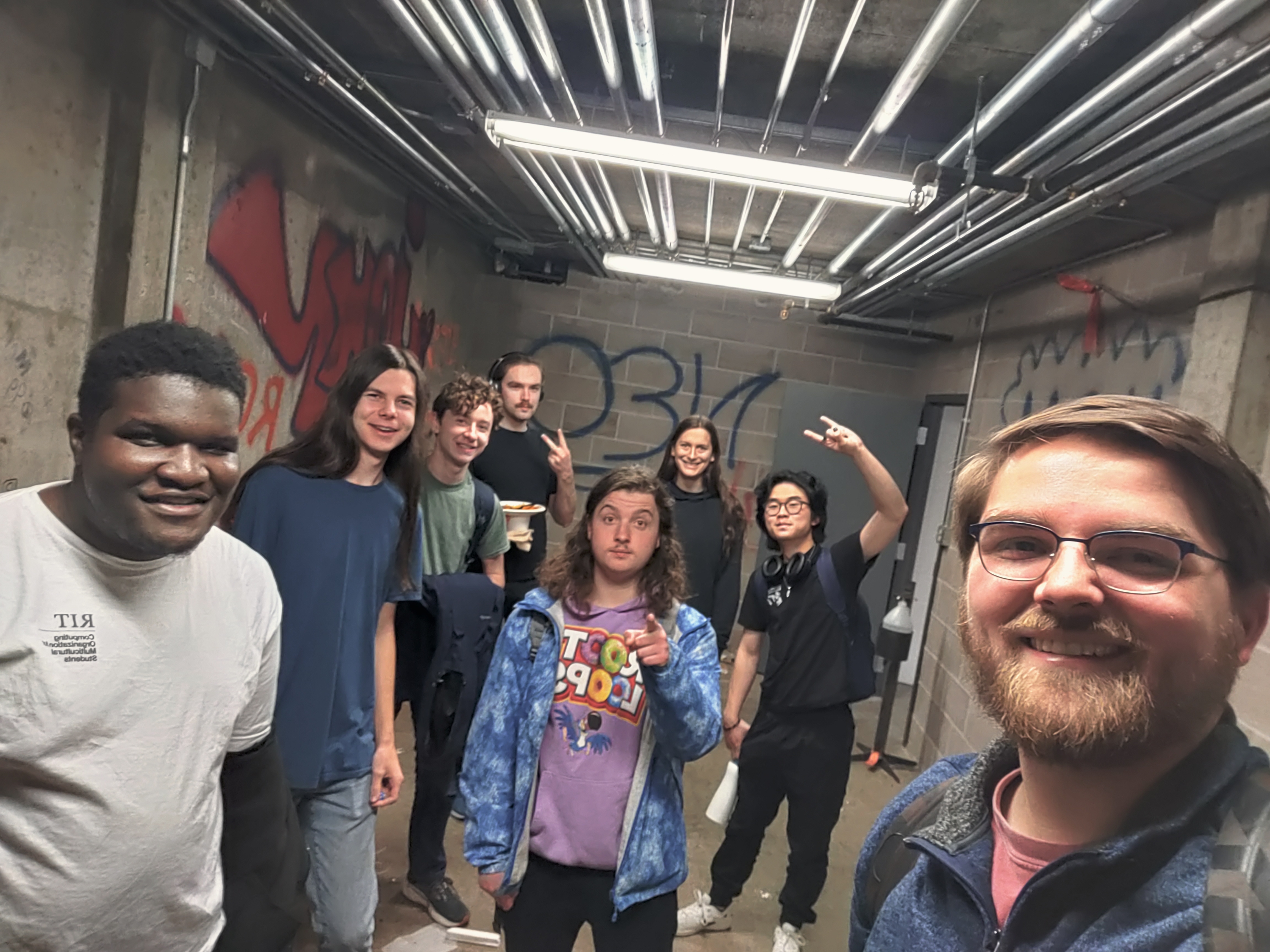 Selfie of six current students in a room with old murals.